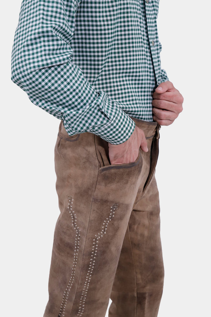 A detailed side view of the man wearing the Addison Oktoberfest Lederhosen Long and green checkered shirt. The focus is on the intricate embroidery along the side of the lederhosen, with one hand in the pocket.