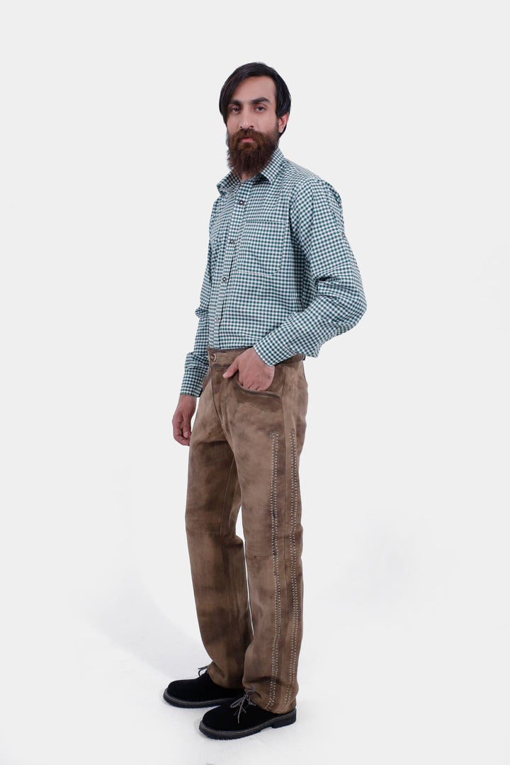 A side view of the man wearing the Addison Oktoberfest Lederhosen Long and a green checkered shirt. The focus is on the lederhosen's detailed side embroidery, with black shoes completing the outfit.