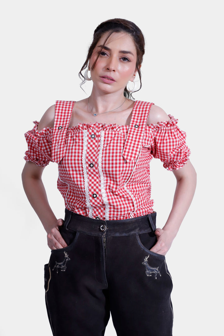 Close-up view of a woman in a red and white checkered off-shoulder blouse with ruffled edges and black lederhosen, showcasing the intricate embroidery on the pants