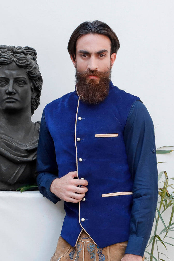 A man wearing a deep blue Bavarian lederhosen vest standing next to a black statue bust. trachtenweste herren​ , trachtenwesten herren​