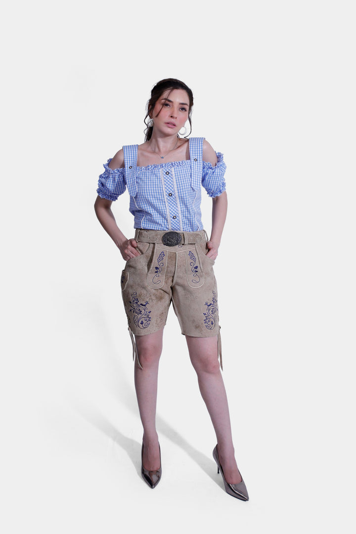  Woman wearing a blue and white checkered off-shoulder top and light brown suede lederhosen with blue embroidery, posing confidently. kurze damen lederhose tracht 