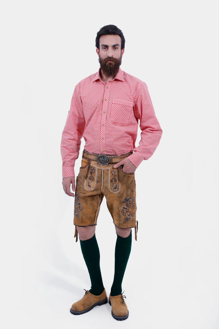 Full-body view of a man wearing Chiemsee Lederhosen with a pink checkered shirt, standing with hands in pockets. Kurze Lederhose Chiemsee mit Hosenträger 