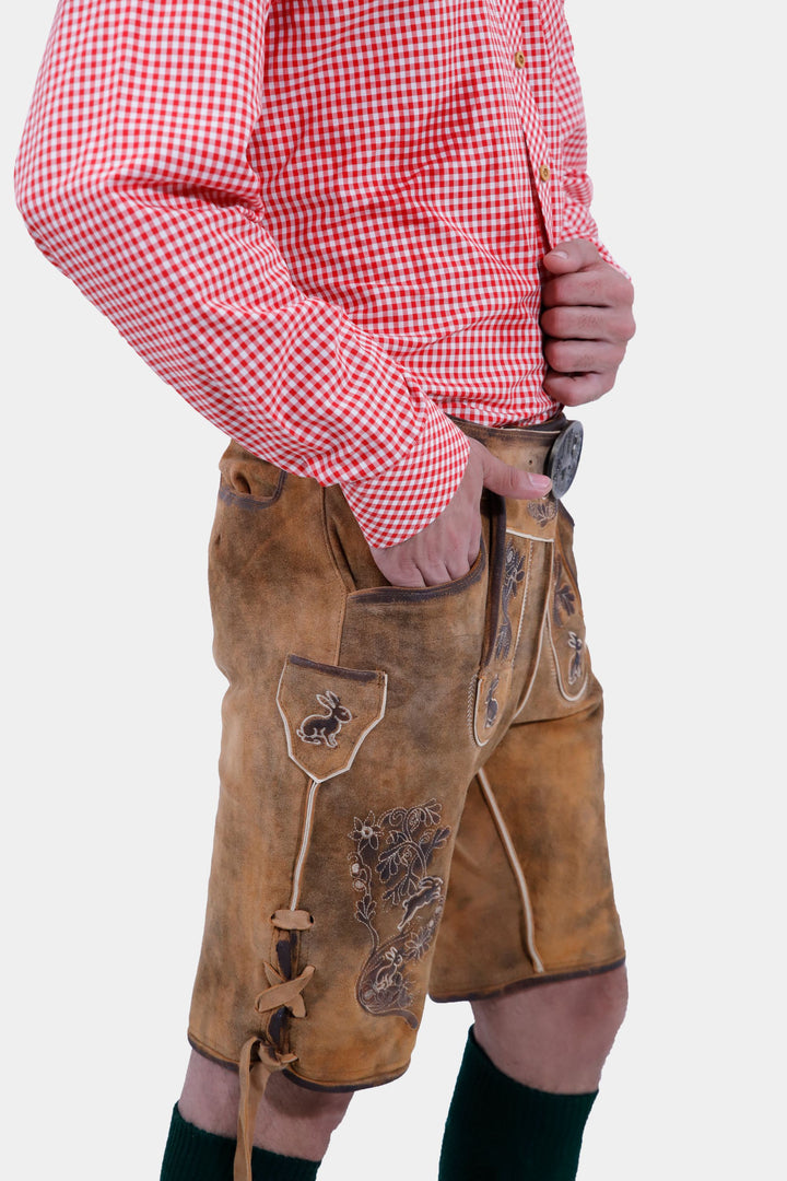 Side view close-up of a man wearing Chiemsee Lederhosen and a pink checkered shirt, highlighting the detailed embroidery and pockets of the leather shorts.