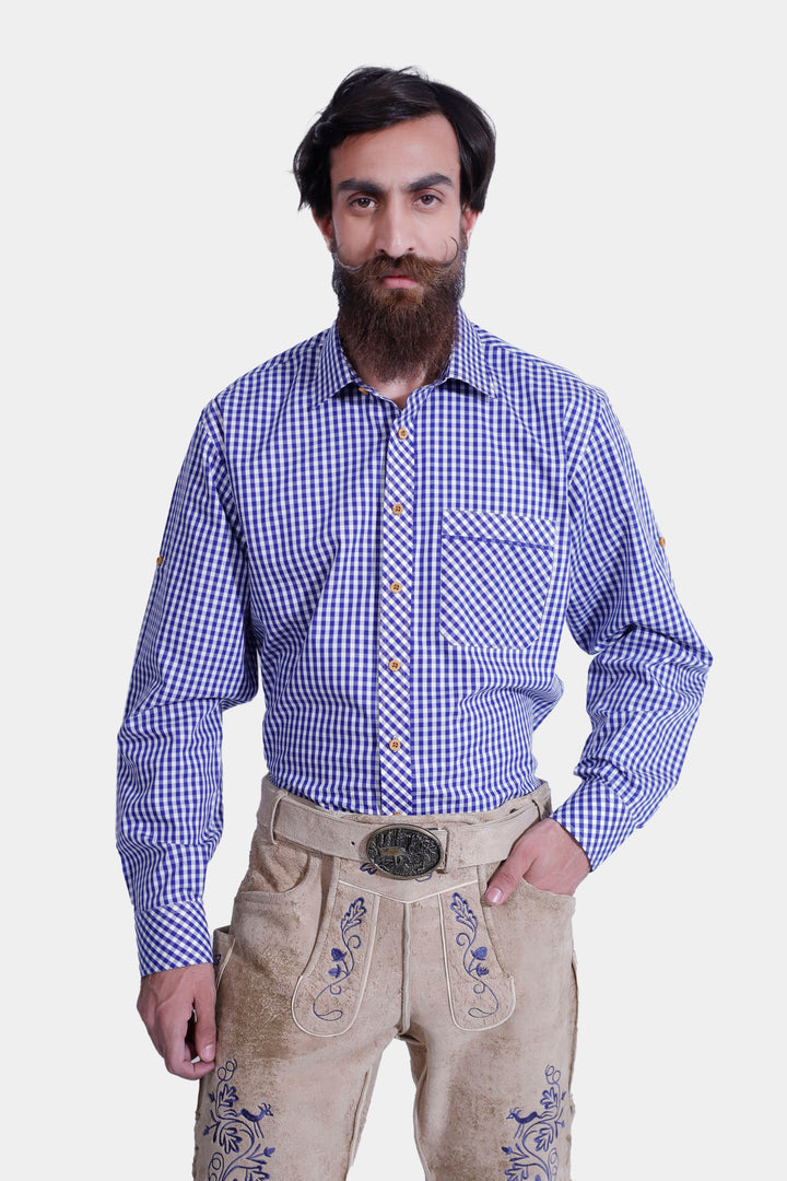 Front view of a man wearing beige-colored Cincinnati Lederhosen with hands in pockets, highlighting the intricate embroidery and traditional Bavarian design. He is also wearing a blue checkered shirt and beige-colored shoes.