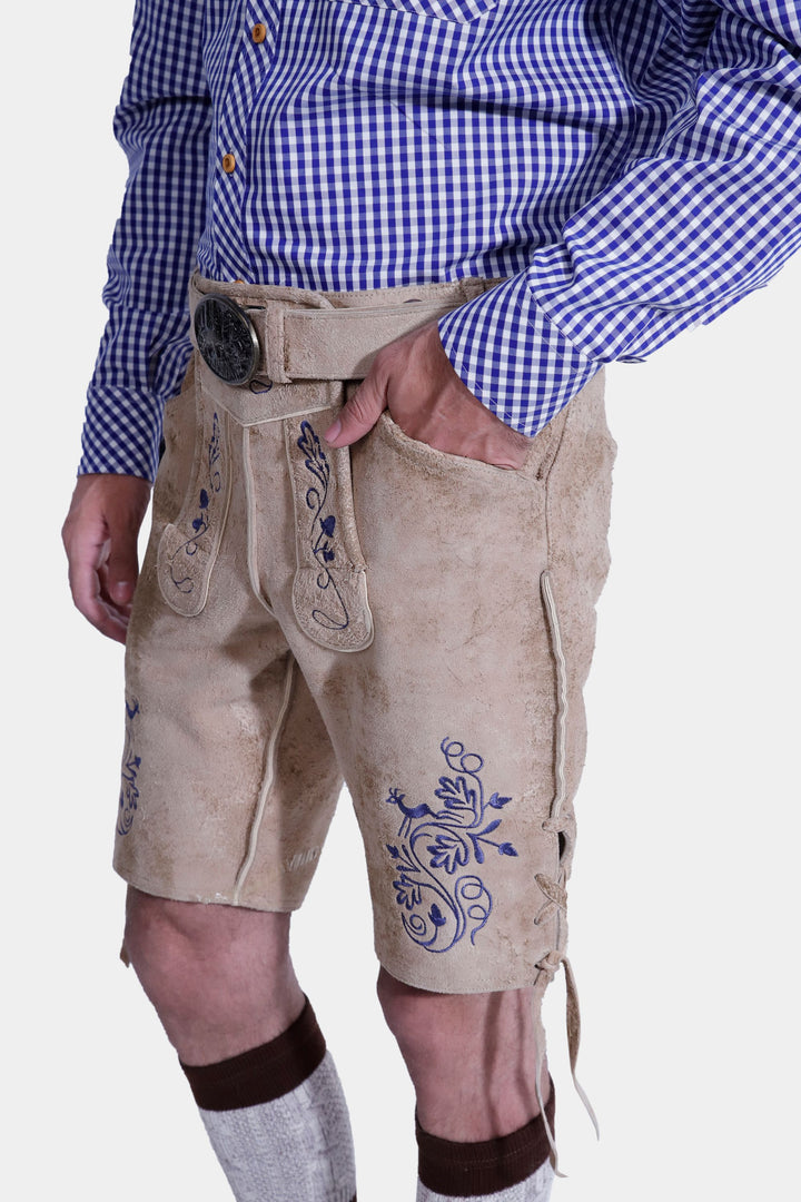 Close-up view of beige-colored Cincinnati Lederhosen, highlighting the intricate embroidery, belt, and craftsmanship of the traditional Bavarian leather shorts. The man is wearing a blue checkered shirt and beige-colored shoes.