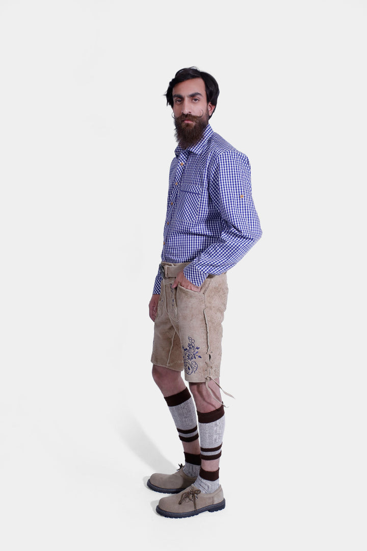 Side profile of a man in beige-colored Cincinnati Lederhosen, emphasizing the leather shorts' design, embroidery, and fit, paired with a blue checkered shirt and beige-colored shoes.