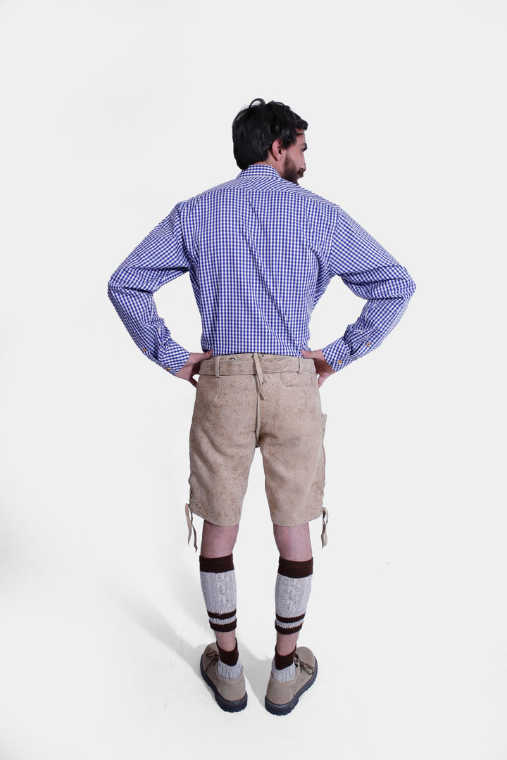 Rear view of a man wearing beige-colored Steuben Lederhosen, highlighting the back pockets and detailed stitching of the traditional Bavarian leather shorts. He is also wearing a blue checkered shirt and beige-colored shoes.