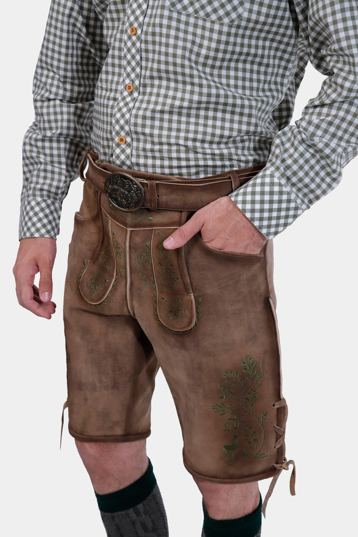 Close-up view of a man wearing a green and white checkered shirt and brown leather lederhosen, focusing on the details of the lederhosen's front pocket and embroidery.