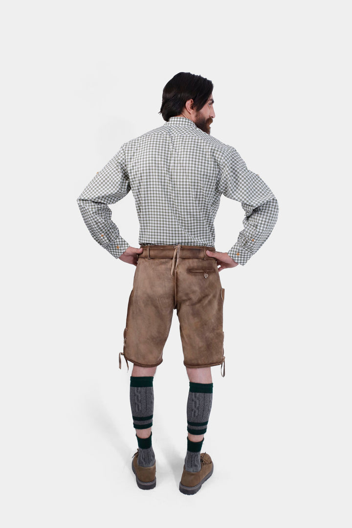 Back view of a man wearing a green and white checkered shirt and brown leather lederhosen, highlighting the back details of the lederhosen.