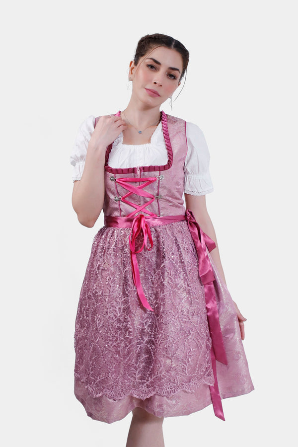 Woman posing thoughtfully in the Dirndl Christiane, featuring a pink lace bodice with intricate detailing and a flowing lace skirt.