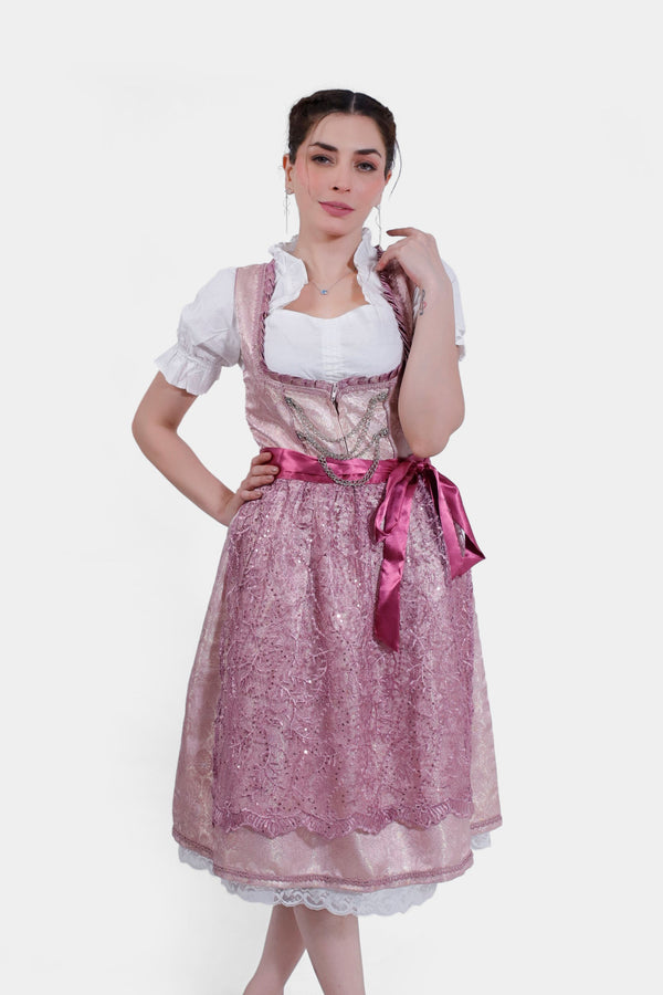 Young woman posing confidently in Dirndl Jessica Schwarz, featuring a delicate pink lace apron over a shimmering rose bodice and skirt.