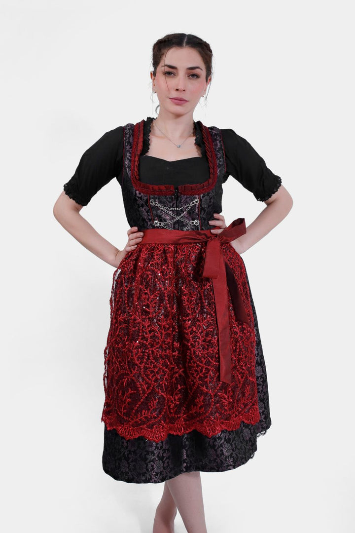 Front view of a woman wearing the Dirndl Kelly, featuring intricate black and red lace detailing with a satin ribbon waistband.