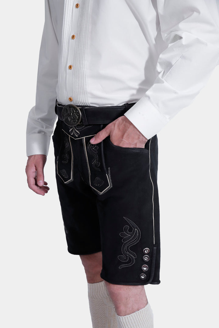 Side view of a man wearing the Elgort Lederhosen Outfit, highlighting the white shirt tucked into black leather Lederhosen with white embroidery and pocket details, along with white knee-high socks.