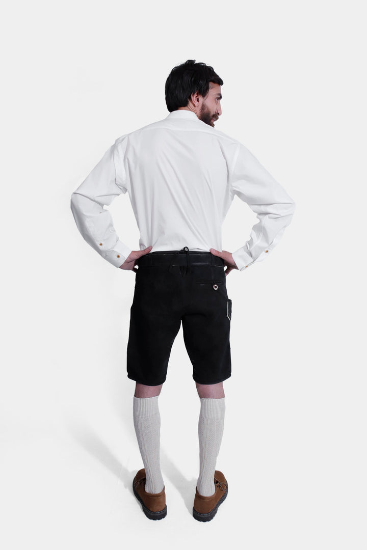 Rear view of a man wearing the Elgort Lederhosen Outfit, featuring a white shirt and black leather Lederhosen with white knee-high socks and brown shoes.