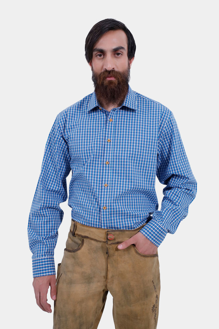 A close-up shot of the man with a beard in a blue checkered shirt and Goretzka lederhosen. He is looking directly at the camera with one hand in his pocket.