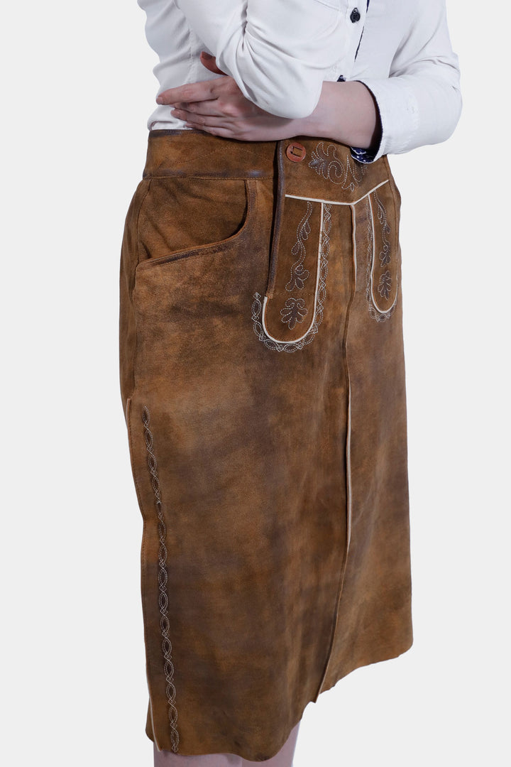 Close-up view of the Griessee Lederhosen Skirt in brown leather worn by a woman, showcasing the intricate white embroidery detail and buttons on the front.