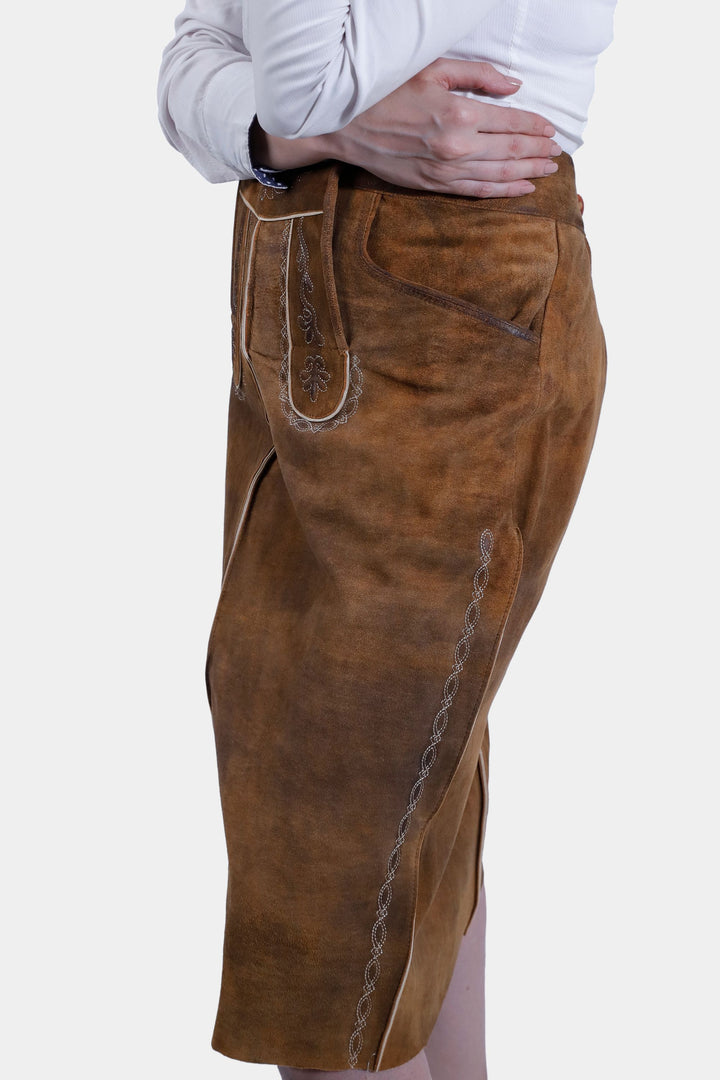 Side view of a woman wearing the Griessee Lederhosen Skirt in brown leather, highlighting the skirt's texture, front flap with embroidery, and side pocket detail.