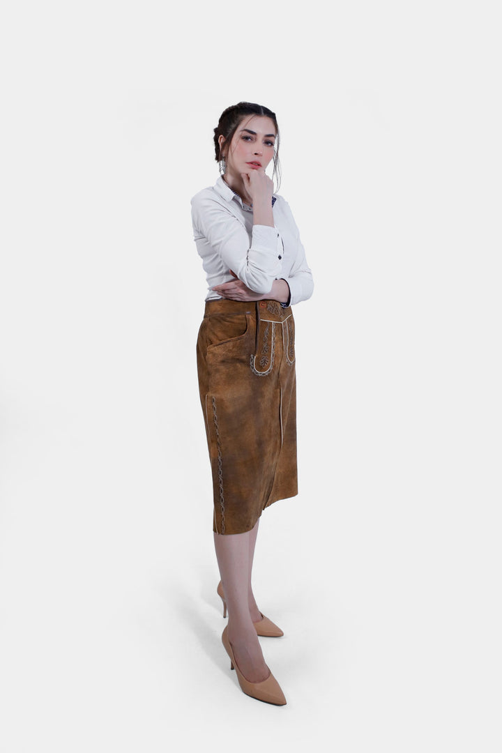 Woman in the Griessee Lederhosen Skirt in brown leather and white button-up shirt, standing with her hand on her chin, showing the skirt's front and side profiles.