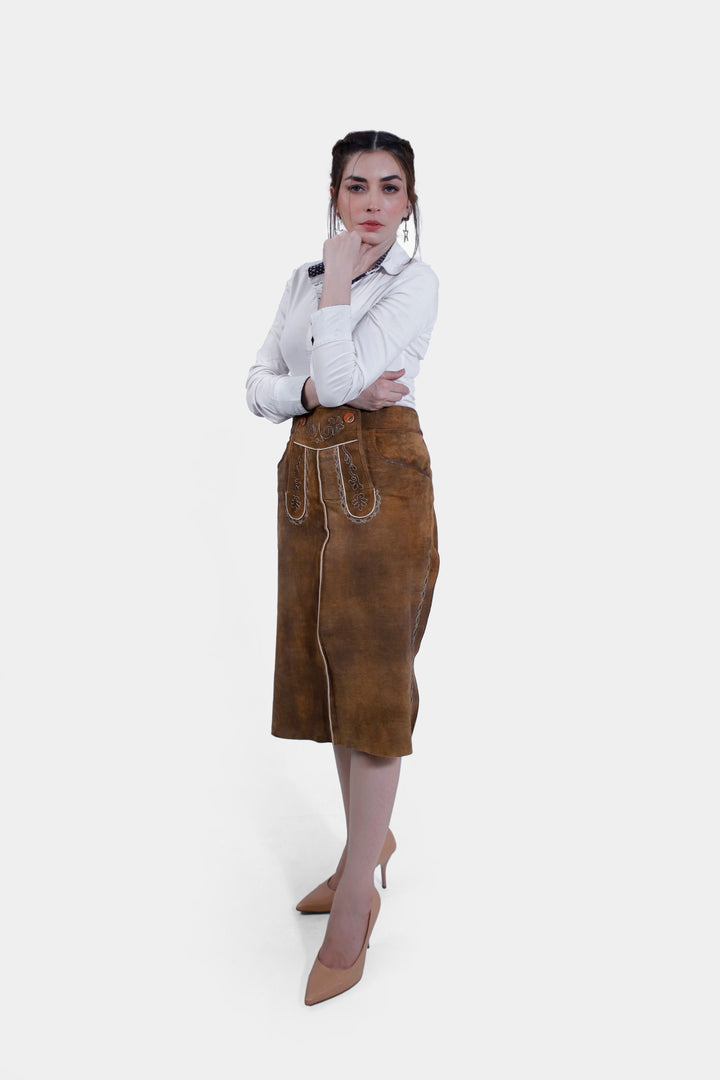 Profile view of a woman in the Griessee Lederhosen Skirt in brown leather, posing with one hand on her chin and the other on her hip, emphasizing the skirt's fit and design.