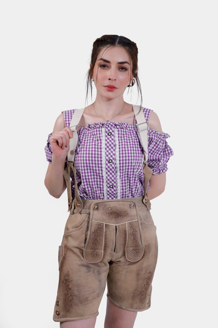 A close-up front view of the woman wearing the Hamburg Lederhosen, focusing on the suspenders and intricate embroidery on the shorts. She is paired with a purple checkered blouse with off-shoulder sleeves and white lace accents.