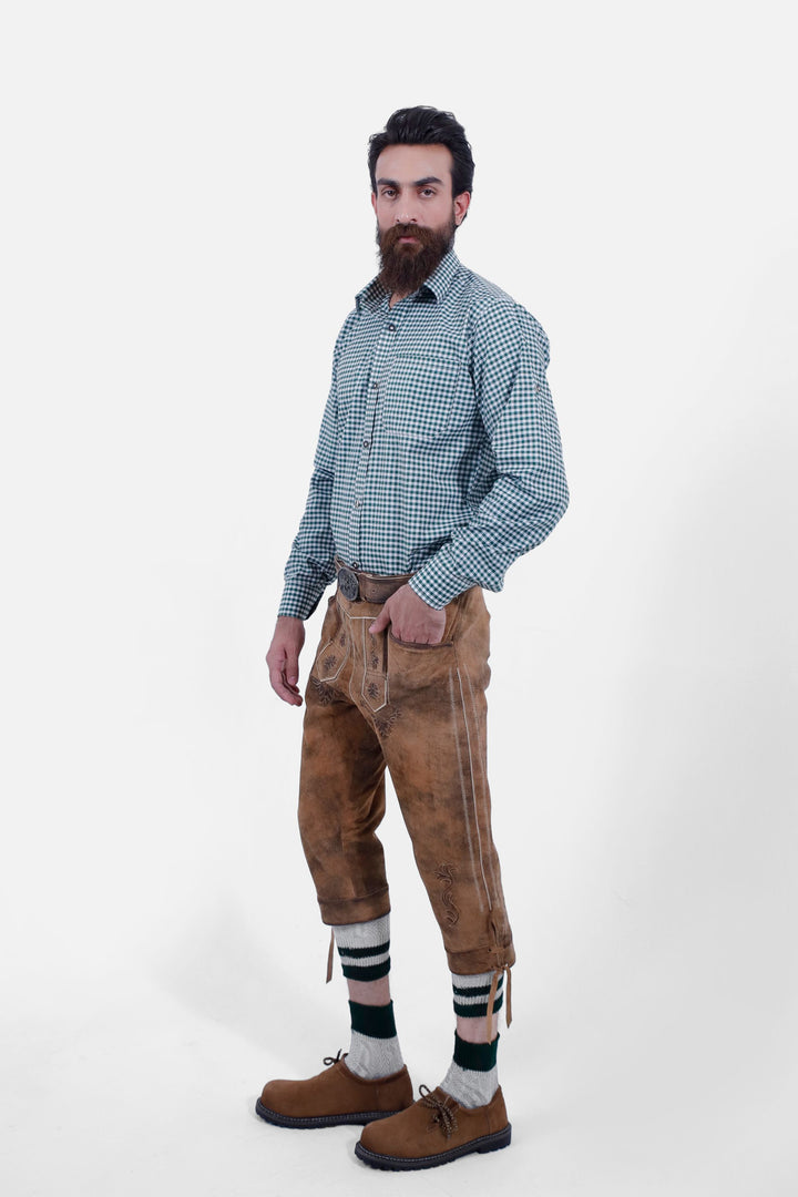 Man dressed in a green checkered shirt and Hesse Bundhosen, posing with a slight side view. The brown leather pants feature intricate floral embroidery, side pockets, and are complemented by traditional Bavarian shoes and green-striped socks.