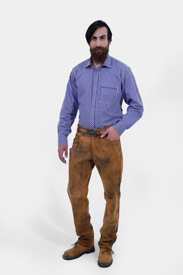 A full-body front view of a bearded man with black hair wearing a blue and white checkered shirt tucked into Humboldt Long Lederhosen, posing with one hand in his pocket and looking at the camera.