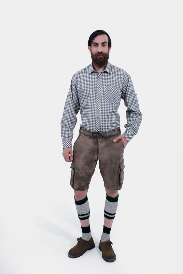 Full-body view of a man wearing Klimt Cargo Lederhosen with a gray checkered shirt, standing with one hand in pocket, showcasing traditional Bavarian attire.  lederhose herren tracht kurz