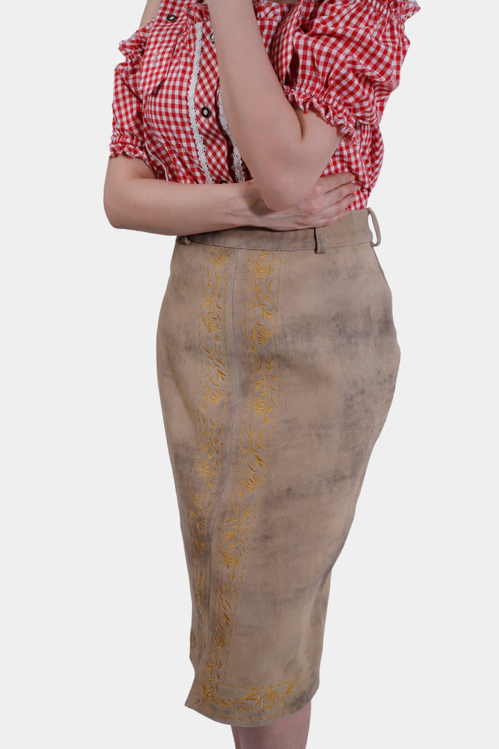 Side view of the Kollwitz Lederhosen Skirt in sandy tan buck skin leather, highlighting the embroidery and fit, worn with a red and white checkered blouse.