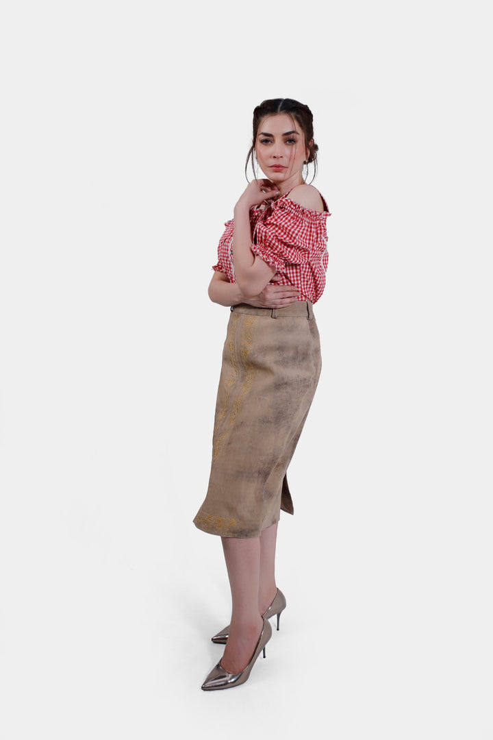 Three-quarter view of the model wearing the Kollwitz Lederhosen Skirt in sandy tan buck skin leather, paired with a red and white checkered blouse.