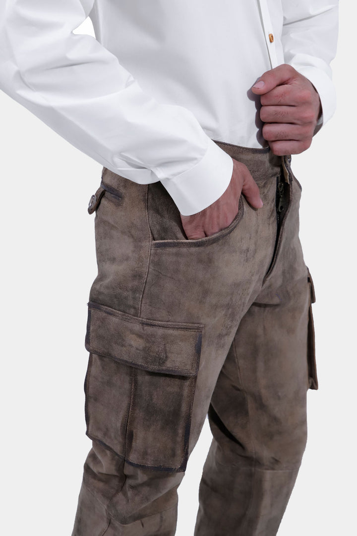 Side view of a person standing with hands in pockets, wearing Königssee Cargo Lederhosen Long Pant with ornate stitching and a white button-up shirt.