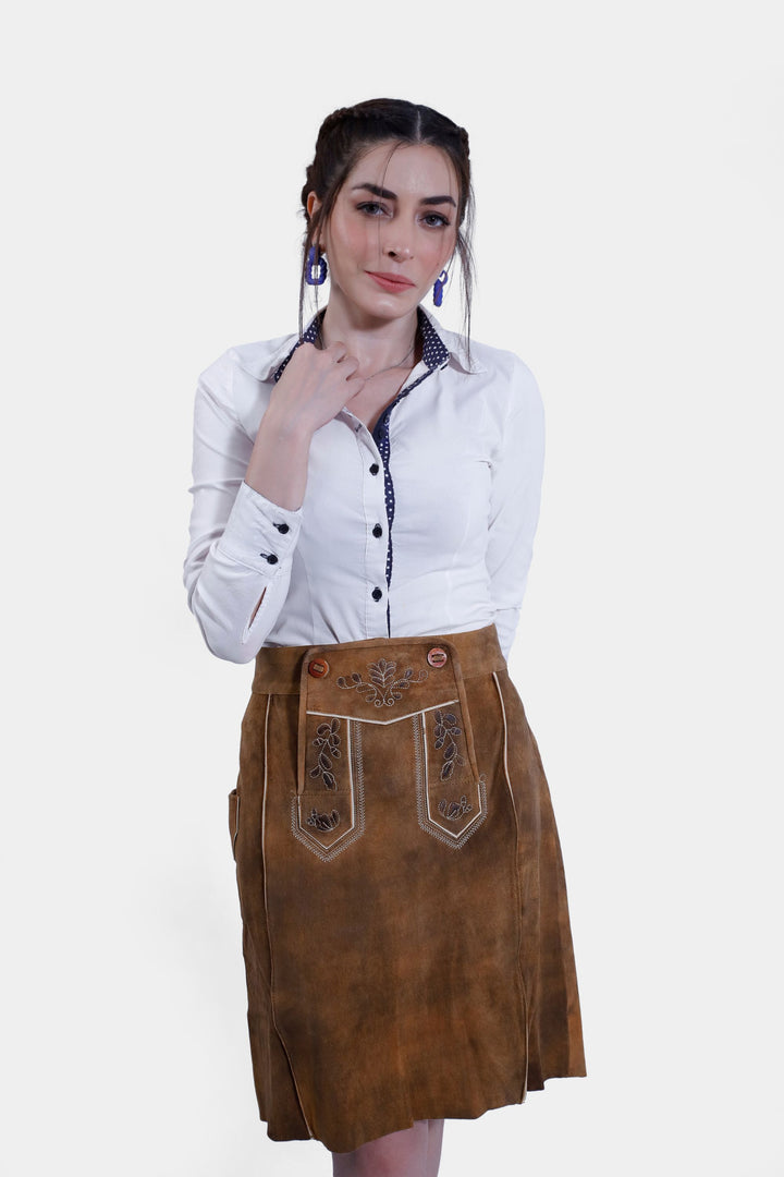 A woman wearing the Marianna Lederhosen Skirt, front view with a slightly different pose. The skirt's brown leather and embroidery are highlighted, paired with a white button-down shirt.