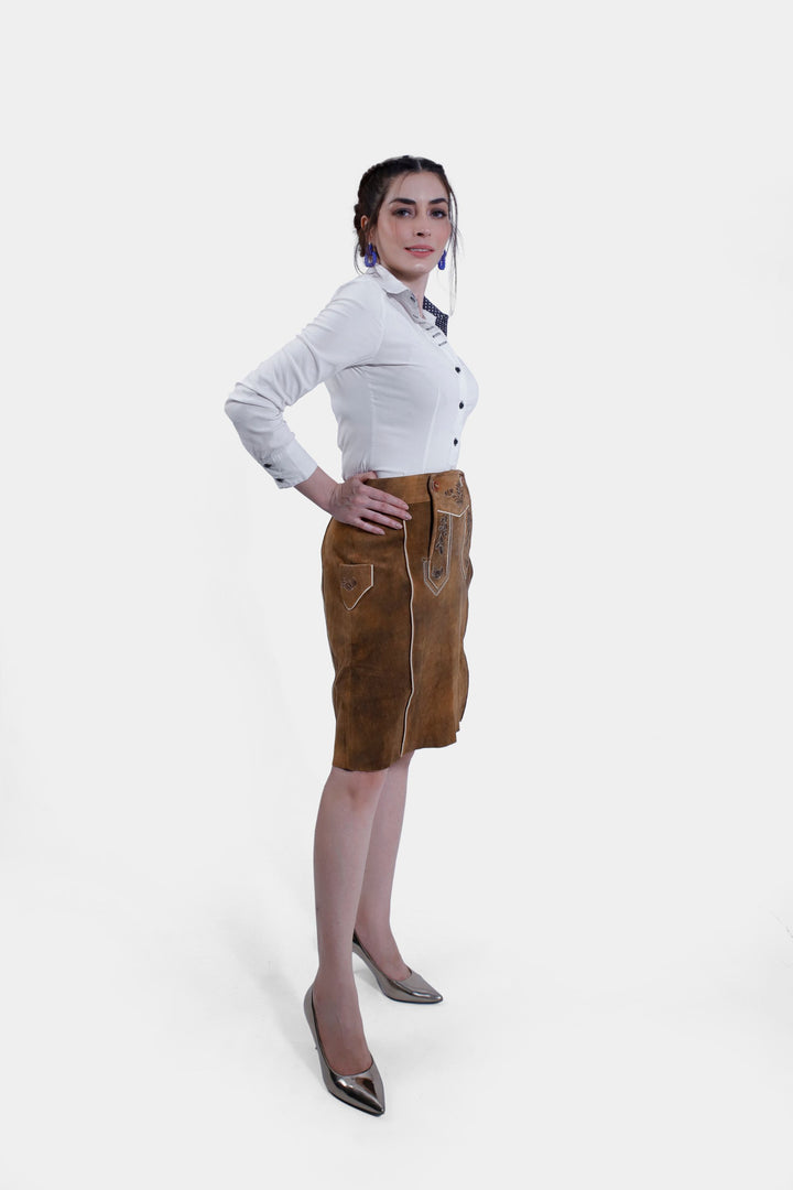 A woman posing in the Marianna Lederhosen Skirt, side view. The skirt features white piping along the seams and detailed embroidery.