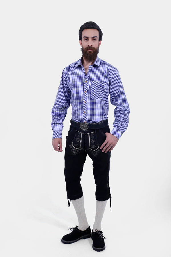 A male wearing a blue checkered shirt and Marx Bundhosen. The Marx Bundhosen features intricate embroidery on the front, a decorative belt buckle, and mid-length. The model's hands are by his sides, and he is wearing black shoes with socks.