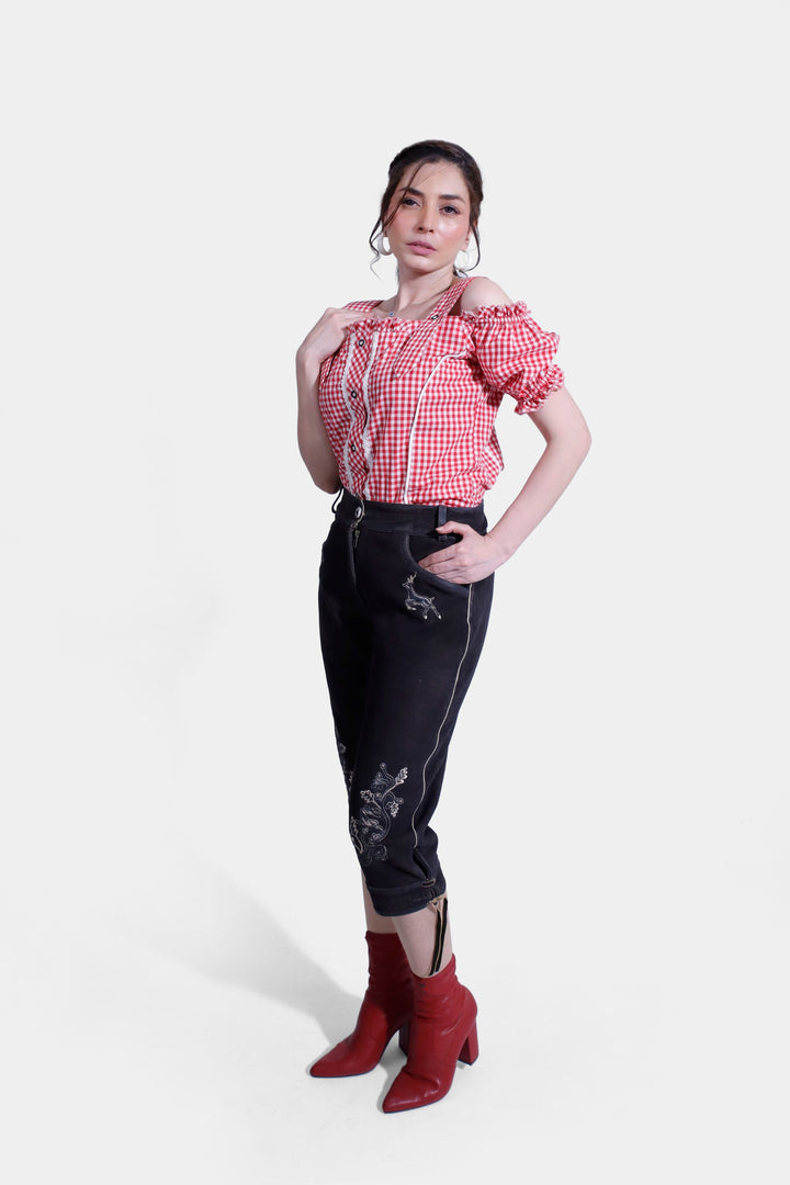 Full-length view of a woman in Midnight Raven Lederhosen and red and white checkered blouse, standing elegantly with a slight turn.