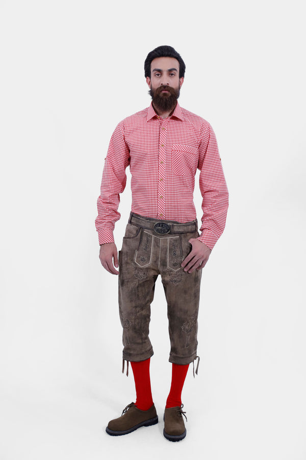 A male wearing a red checkered shirt and Milwaukee Old World Bundhosen. The Milwaukee Old World Bundhosen features intricate embroidery on the front, a decorative belt buckle, and mid-length. The model's hands are by his sides, and he is wearing brown shoes with red socks.