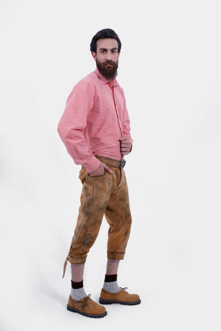 A bearded man wearing a white patterned shirt and Miroslav Klose Bundhosen Outfit, posing with his hand in his pocket. The lederhosen features detailed embroidery on legs, paired with traditional socks and brown shoes.