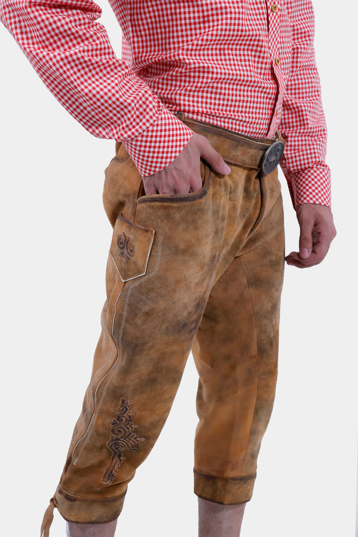 Side view of tan brown Miroslav Klose Bundhosen Outfit featuring embroidery on legs and lases on cuffs, worn by a man against a white background.