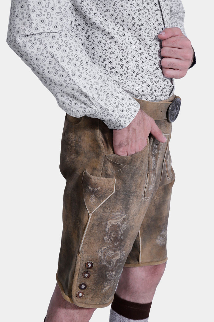 Three-quarter view of a man in Mozart Lederhosen, showcasing the fit and traditional Bavarian style with embroidered details. The man is wearing a white patterned shirt and beige shoes.