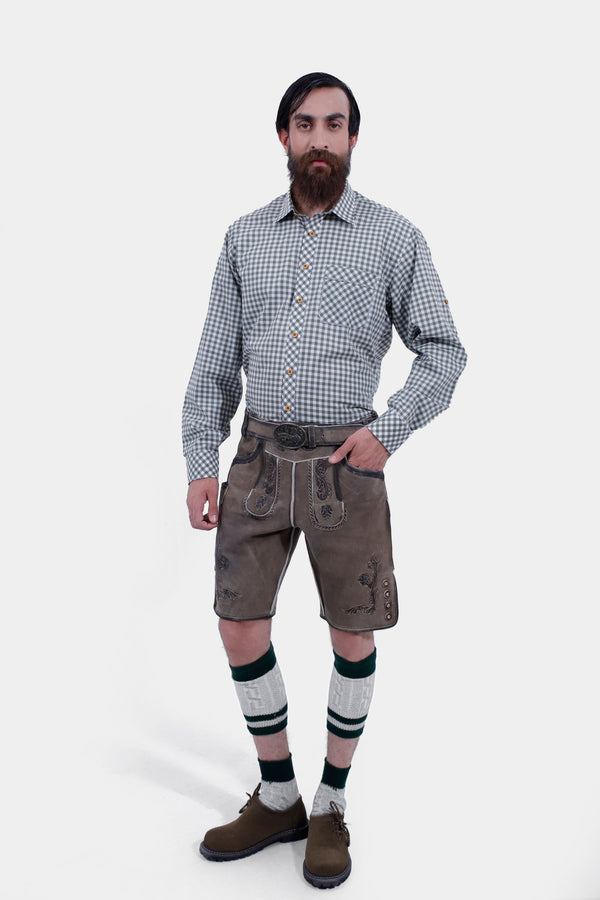 Full-body view of a man wearing Salzburg Fortress Lederhosen with a gray checkered shirt, standing with one hand in pocket, showcasing traditional Bavarian attire.