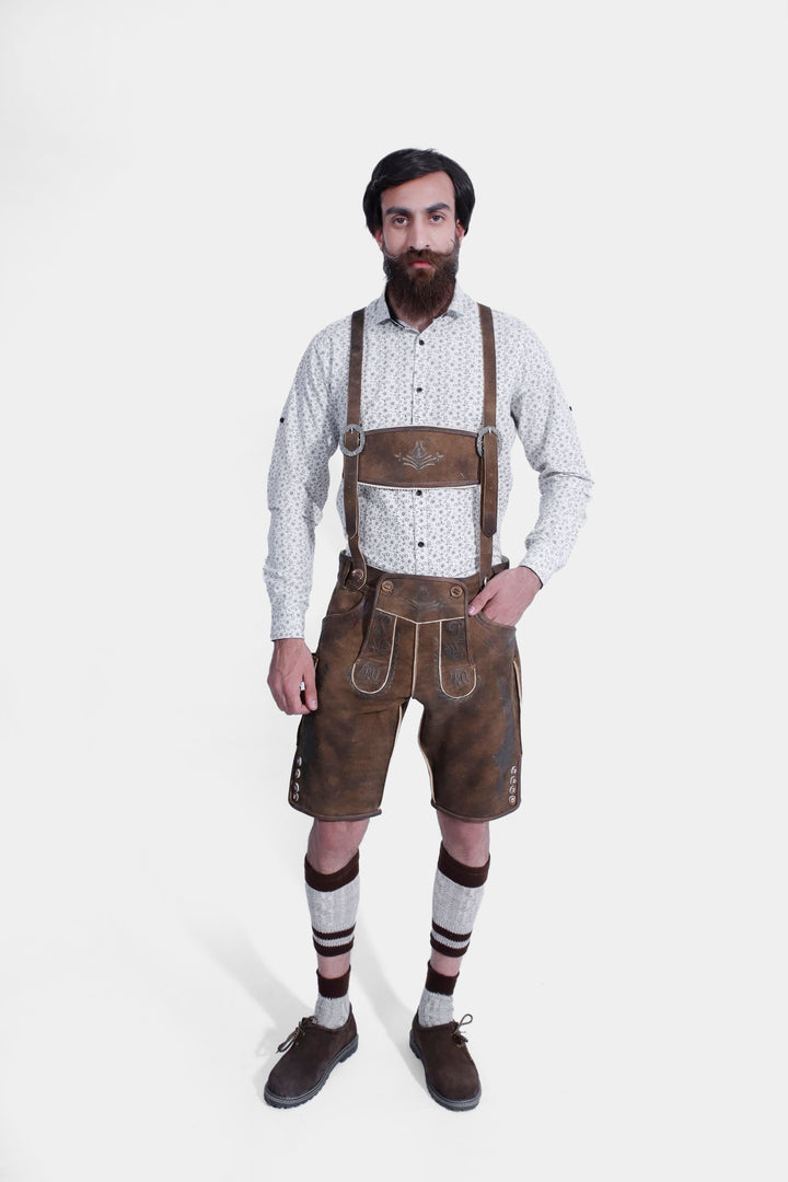 Full view of brown leather lederhosen with attached suspenders, showcasing detailed embroidery and buttons, worn by a man against a white background.