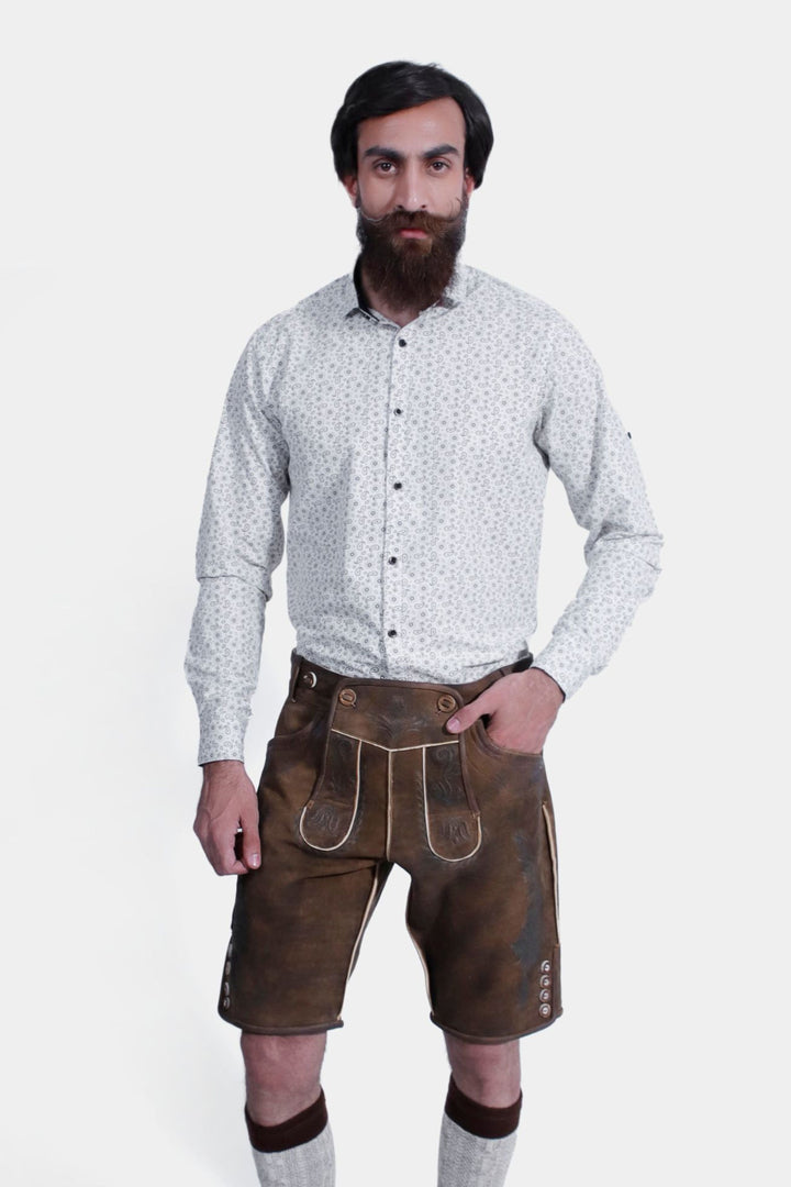 Close-up of brown leather lederhosen showcasing detailed embroidery and buttons, worn by a man against a white background.