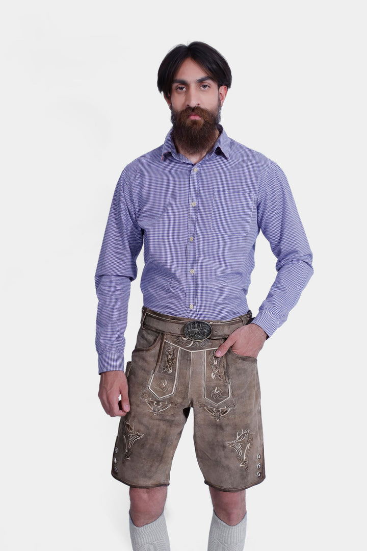 Close-up of a man in a Ski Amadé Lederhosen Outfit, highlighting the detailed embroidery on brown leather shorts and blue checkered shirt.