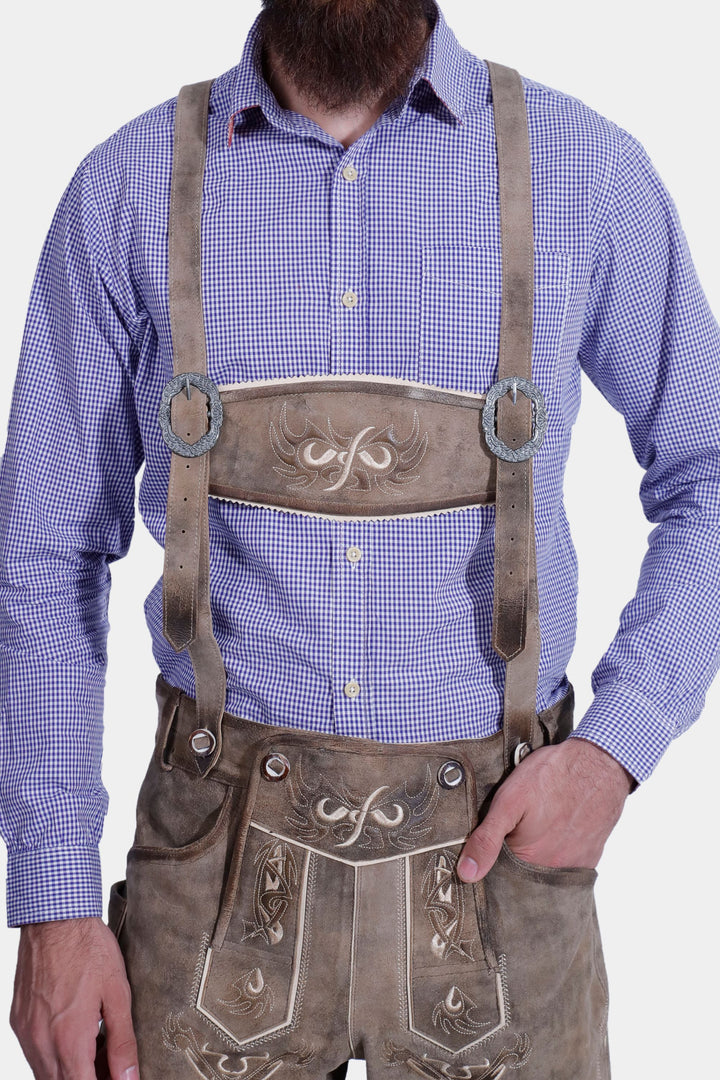 Close-up of a man in a Ski Amadé Lederhosen Outfit, highlighting the detailed embroidery on brown leather shorts and blue checkered shirt.