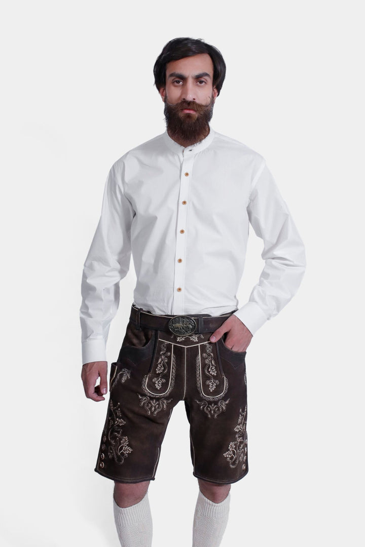 Front view of a model in Spiegel Lederhosen, focusing on the detailed embroidery and traditional design of the leather shorts, with a white button-down shirt.