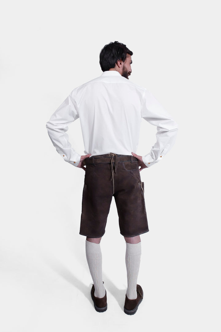 Full-body view of a model from the back wearing Spiegel Lederhosen, displaying the plain back design of the leather shorts and the white shirt.