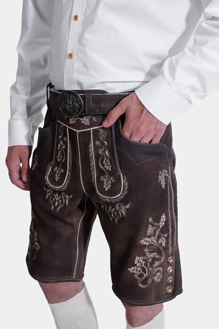 Close-up of a man wearing a traditional white Bavarian shirt and brown Spieth Lederhosen outfit with intricate embroidery, his hand resting in the pocket