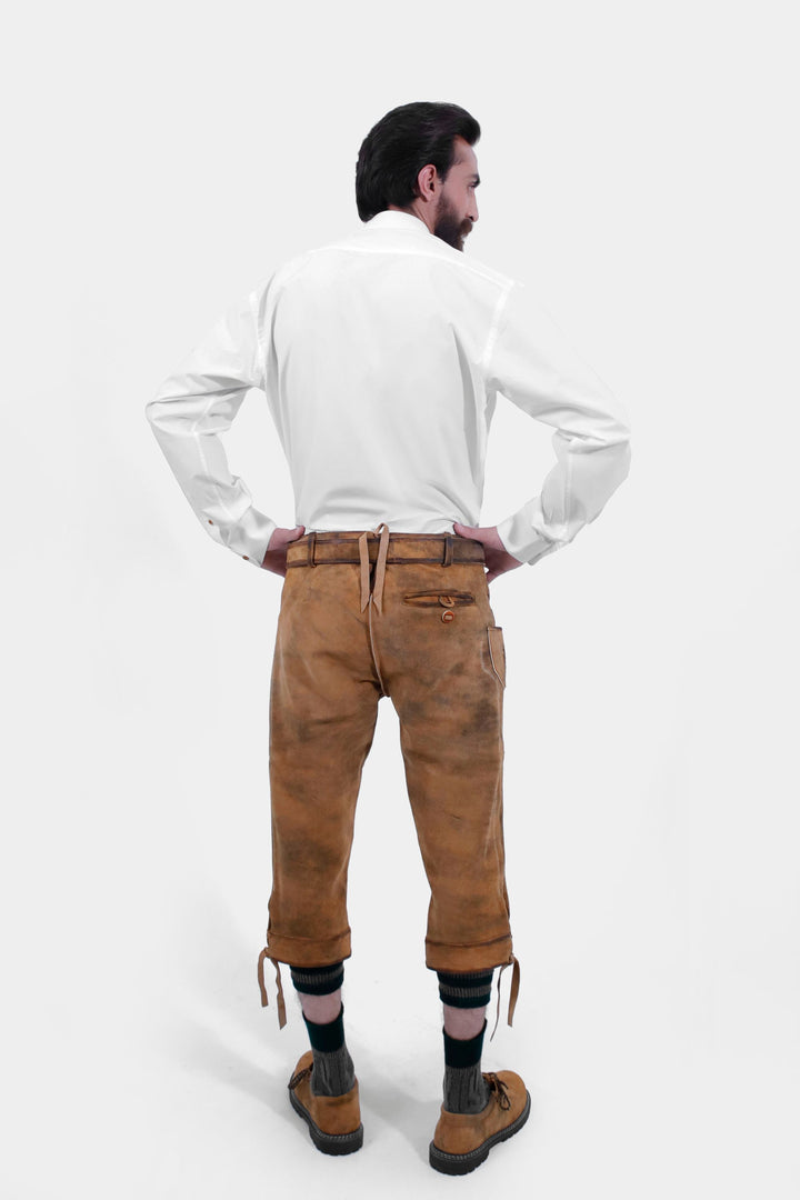 Rear view of a man wearing Tegernsee Bundhosen. He is dressed in a white traditional shirt and brown bundhosen with detailed embroidery, showcasing the back design.