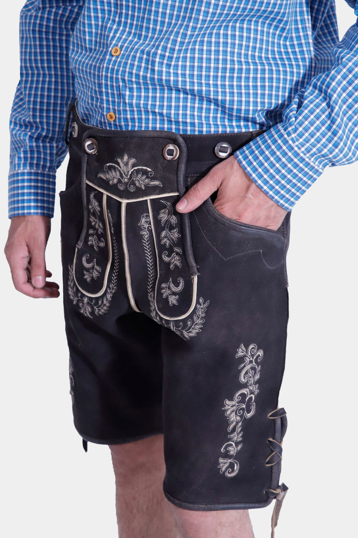  Side view of a man wearing the Timothée Lederhosen Outfit, showing the blue checkered shirt tucked into black leather Lederhosen with white embroidery and a side pocket detail.