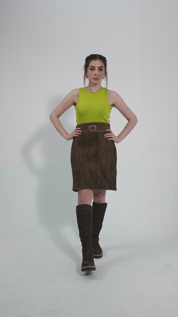 video featuring a model elegantly showcasing a traditional brown leather skirt paired with a vibrant yellow sleeveless top. The model poses from various angles to highlight the skirt's rustic texture and chic buckle detail. The video emphasizes the skirt's fusion of traditional craftsmanship and modern style, making the Leni Lederhosen Skirt a versatile piece for both casual and festive occasions.