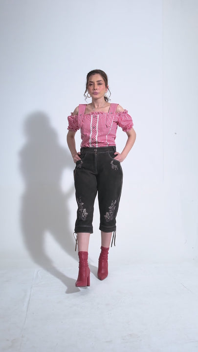 Showcase video of the Alex Morgaan Lederhosen Outfit, featuring a model walking and turning in various poses to highlight the detailed embroidery and stylish fit of the lederhosen. The video captures the versatile appeal of the lederhosen from different angles, paired with a chic red and white blouse and stylish red boots.